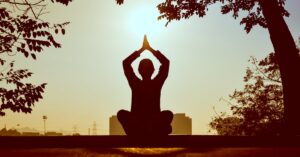 Silhouette of a person practicing yoga outdoors during sunrise, creating a calming atmosphere.